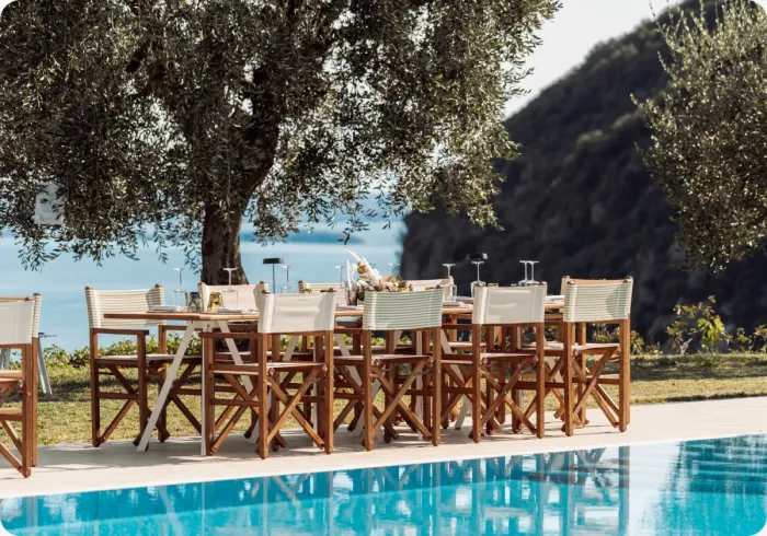Tavolo apparecchiato a bordo piscina sotto un ulivo